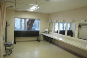 右側に5枚の鏡が設置された化粧台があり、机と椅子が積み重ねて壁側に置かれている楽屋2の写真