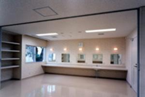 前方に5枚の鏡が設置された化粧台があり、左側には4段の棚がある楽屋2の写真