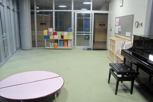 床はカーペットが敷かれ、ピアノや絵本、円形のテーブルが設置されている子供室の写真