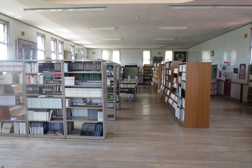 2階閲覧スペース。広い空間に並ぶ書棚と奥に机と椅子が並ぶ。